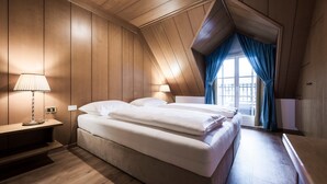 A bedroom with a wooden ceiling, a bed with white bedding, a nightstand with a lamp, and a window with blue curtains.