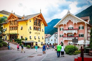 Kaupunginaukio, jota reunustavat historialliset rakennukset, mukaan lukien hotelli nimeltä ’CAVALLINO Bianco’ ja rakennus, jonka kyltissä lukee ’ADLER 1810’.