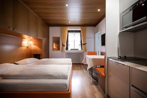 A hotel room with two beds, a kitchenette, and a window with curtains. - "Villa Stella Apartment N 76" near the ski lifts with Wi-Fi and garden (St.Ulrich)