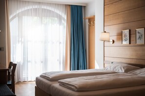 Une chambre d’hôtel avec deux lits, un bureau, une chaise, une grande fenêtre avec des rideaux légers et une lampe fixée au mur.