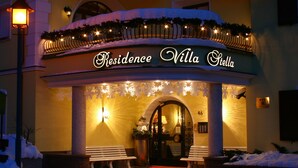 A hotel entrance with a sign reading 'Residence Villa Stella,' two benches outside, and a red carpet leading to the door.