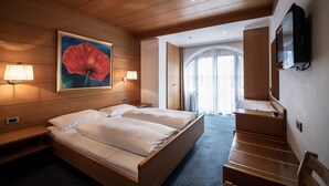 A hotel room with a wooden bed, two bedside lamps, a TV, and a large painting of a flower.