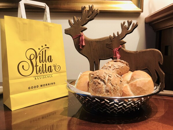 A yellow bag with 'Villa Stella' branding, a wooden reindeer decoration, and a basket of bread.