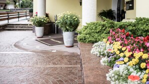 A hotel entrance with a sign reading 'Villa Stella,' a curved facade, columns, potted plants, and a flower bed.