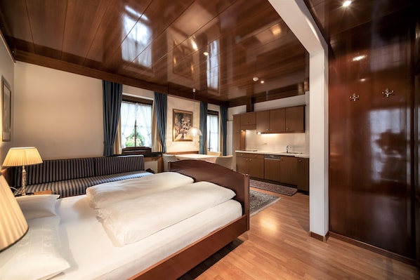 Ein modernes Hotelzimmer mit einem großen Bett, einer Sitzecke, einer Küchenzeile und Blick ins Freie.