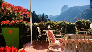 Un patio con mobiliario exterior, una maceta verde con un símbolo de corazón y vistas a la montaña.