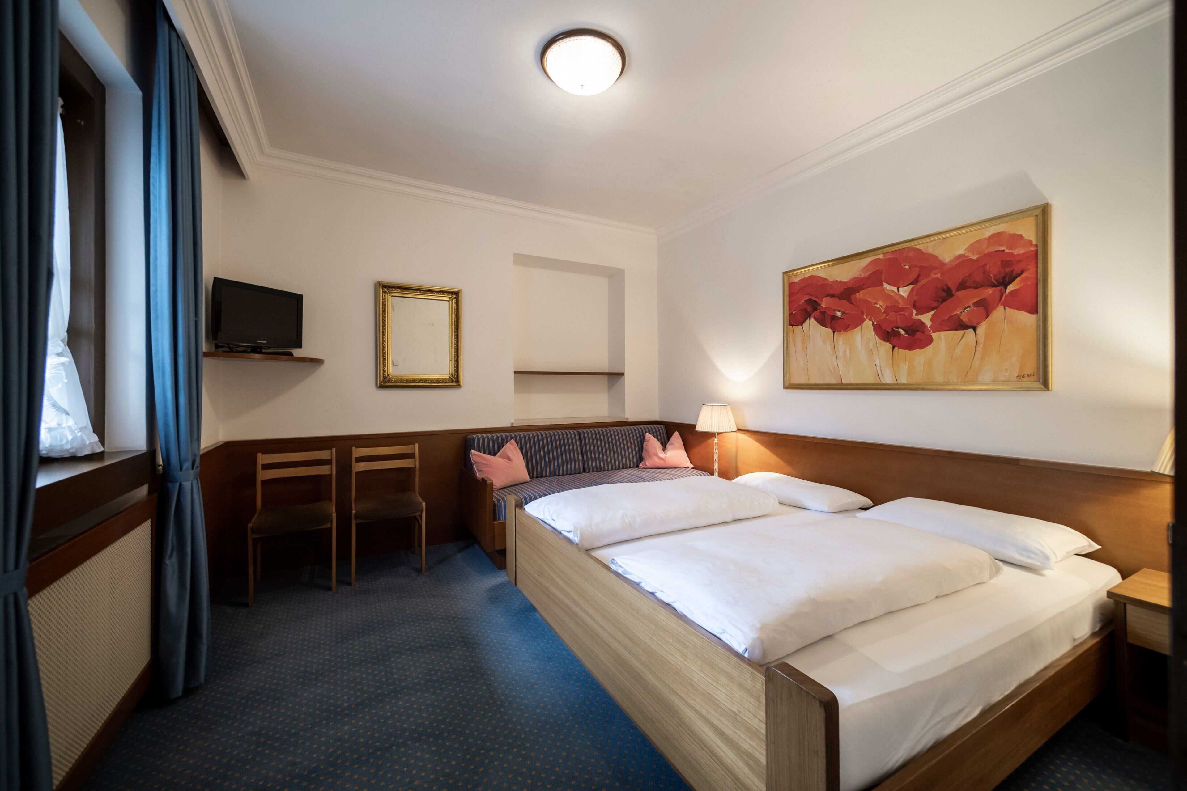Habitación de hotel con cama, escritorio, silla, televisor y un cuadro en la pared.