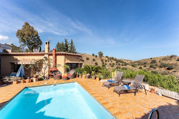 A pool area with lounge chairs and a view of a hillside.
