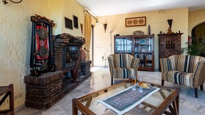 A living room with a fireplace, striped armchairs, a glass coffee table, and a bookshelf. - Villa 'Cosy House Jacuzzi Wifi Pool View' with Sea View, Wi-Fi and Air Conditioning (Mijas Pueblo)