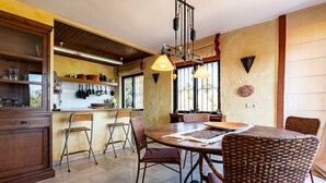 A kitchen with a dining table, wicker chairs, and hanging pots. - Villa 'Cosy House Jacuzzi Wifi Pool View' with Sea View, Wi-Fi and Air Conditioning (Mijas Pueblo)