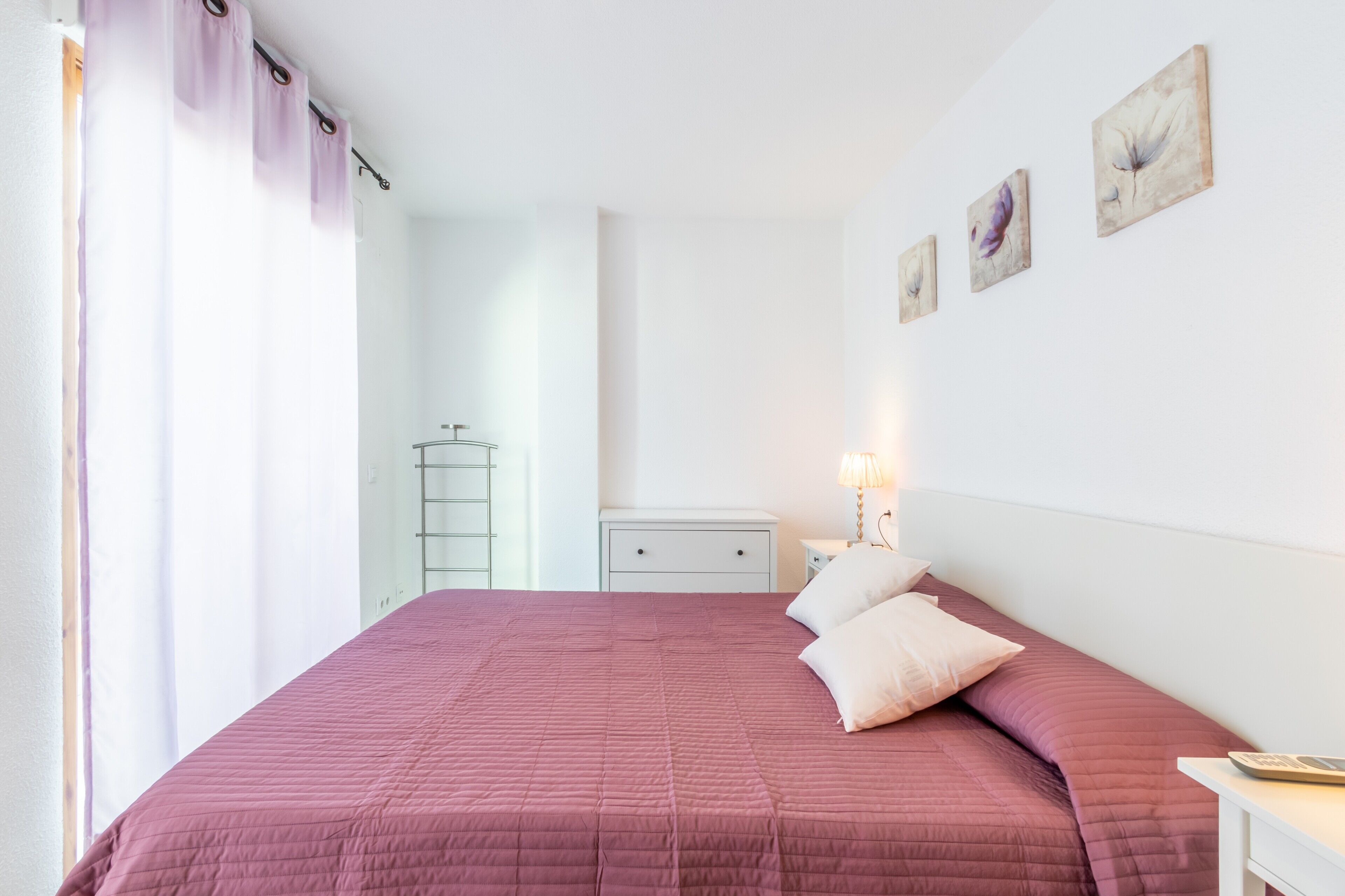 Un dormitorio con una cama grande, una mesita de noche, un armario y una lámpara de pared.