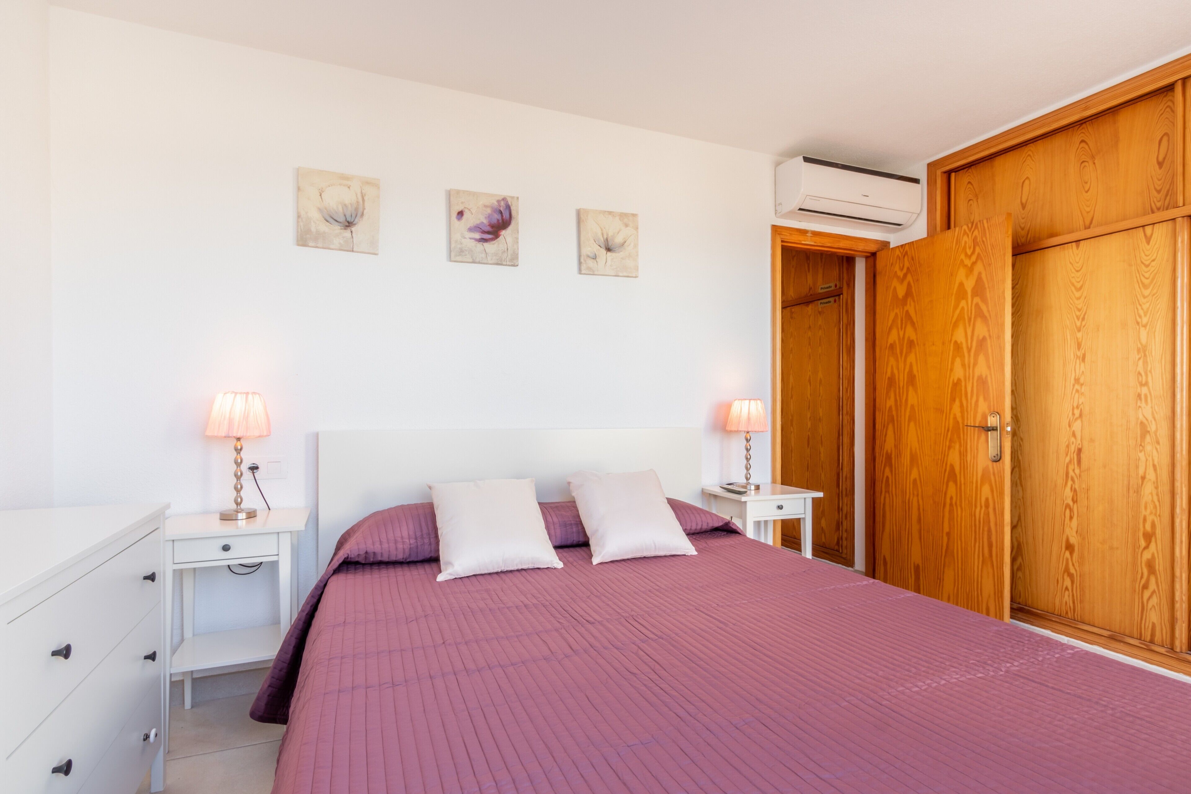 A bedroom with a bed, two bedside tables, a dresser, a wardrobe, and wall art.