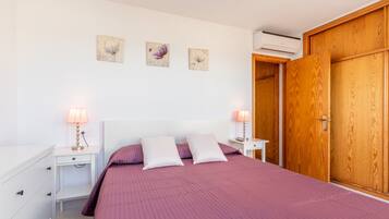 A bedroom with a bed, two bedside tables, a dresser, a wardrobe, and wall art.