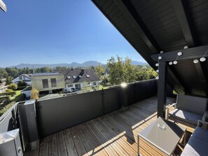 A wooden deck with outdoor furniture, a view of houses and mountains, and string lights. - Nettenwiesen "Charme" Vacation Apartment in Balingen-Endingen (Balingen)