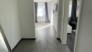 Un hall d’entrée spacieux, doté d’un sol carrelé, qui mène à une chambre avec une grande fenêtre et des rideaux.