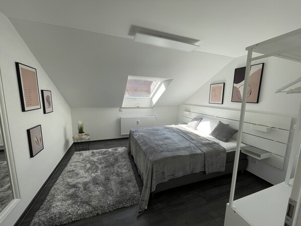 A bedroom with a sloped ceiling, a skylight, a bed with a grey bedspread, a fluffy rug, and framed pictures on the walls. - Nettenwiesen "Charme" Vacation Apartment in Balingen-Endingen (Balingen)