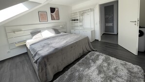 Une chambre moderne avec un plafond en pente, un grand lit avec une literie grise, un tapis moelleux et un dressing.