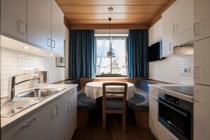 A compact kitchen with a dining area, built-in appliances, and a window with curtains.
