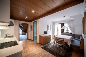 A compact living space with a kitchenette, a dining area with a table and chairs, a sofa, and a window with curtains. - Villa Stella Apartment N 56 near the ski lift with mountain view and garden (St.Ulrich)
