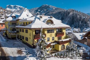 A yellow building with balconies and a snow-covered roof, surrounded by snow and mountains. - Villa Stella Apartment N 56 near the ski lift with mountain view and garden (St.Ulrich)