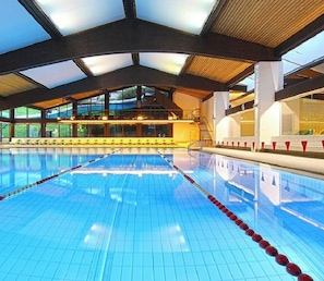 Piscina interior com pistas demarcadas, teto alto e grandes janelas.