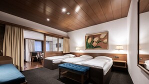 Une chambre d’hôtel avec deux lits, un banc bleu, un bureau et un tableau représentant des fleurs.