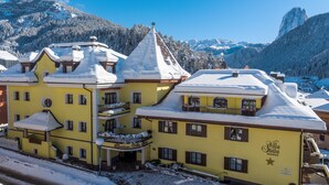 Un edificio amarillo con varios balcones y un techo cubierto de nieve, rodeado de montañas.