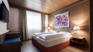 Una habitación de hotel con cama, mesitas de noche, televisión, ventana con cortinas y un cuadro en la pared.