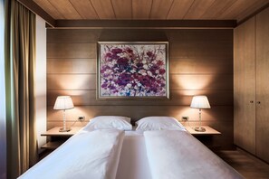 Un letto matrimoniale con due comodini, ognuno dotato di una lampada, in una stanza con pannelli di legno e un'ampia opera d'arte floreale sopra il letto.