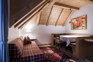 Et hyggeligt rum med skrå vægge, en sofa, et spisebord og et mønstret tæppe.
