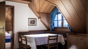Una habitación con techo inclinado, una mesa con sillas, una cama y una ventana con cortinas.