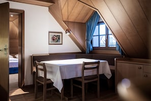 A room with a sloped ceiling, a table with chairs, a bed, and a window with curtains.