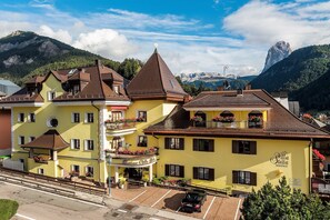 Um edifício amarelo com varanda e uma placa com a inscrição 'Villa Stella Residence', com montanhas ao fundo.