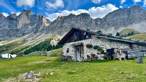 Una cabaña rústica de montaña con fachada de piedra, techo de madera y un pequeño porche.