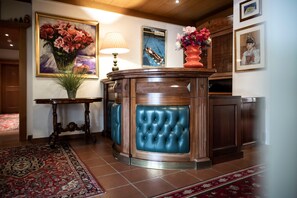 Um hall com um balcão de madeira, um banco acolchoado azul, um tapete estampado e uma pintura de flores.