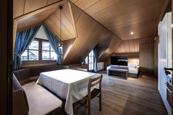 A modern loft bedroom with a sloped ceiling, a large bed, a seating area with a table, and a TV in the corner.