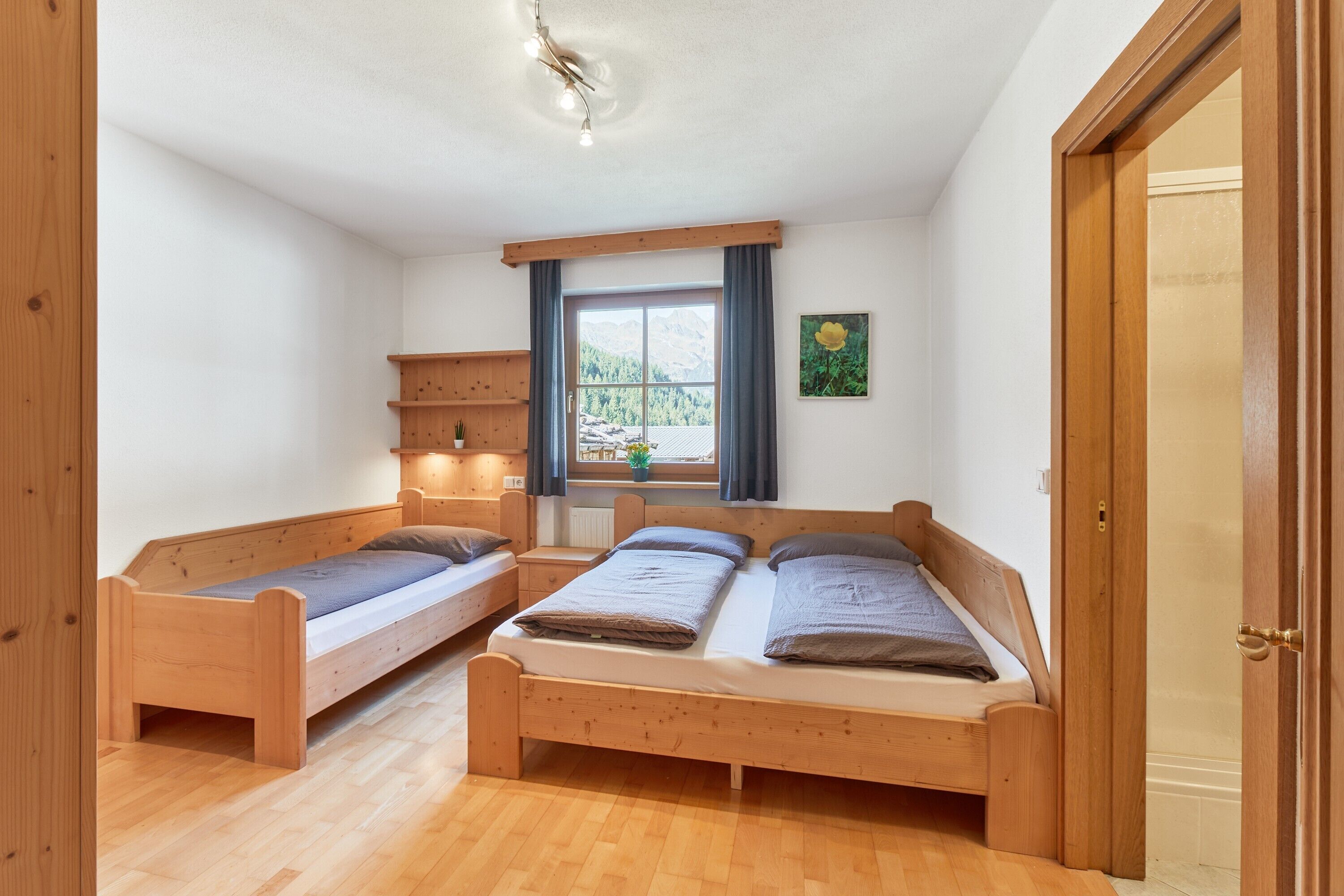 Een kamer met twee houten bedden, een raam met gordijnen, een klein plankje en een deur.