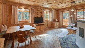 Interior d'una cabana de fusta amb una taula de dinar, cadires, un televisor i un sofà.