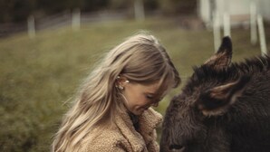 Uma pessoa interagindo com um burro em um ambiente natural, com montanhas ao fundo.