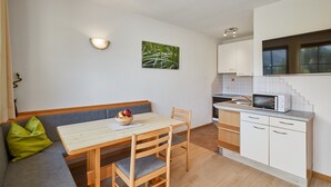 Een kleine keuken met een eettafel, houten stoelen, een magnetron en een klein raam.