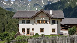 Een huis met twee verdiepingen, een balkon, een houten hek en een bergachtige achtergrond.