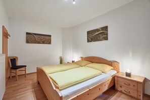 Une chambre à coucher avec un lit en bois, une chaise, une table de chevet et deux tableaux accrochés au mur.