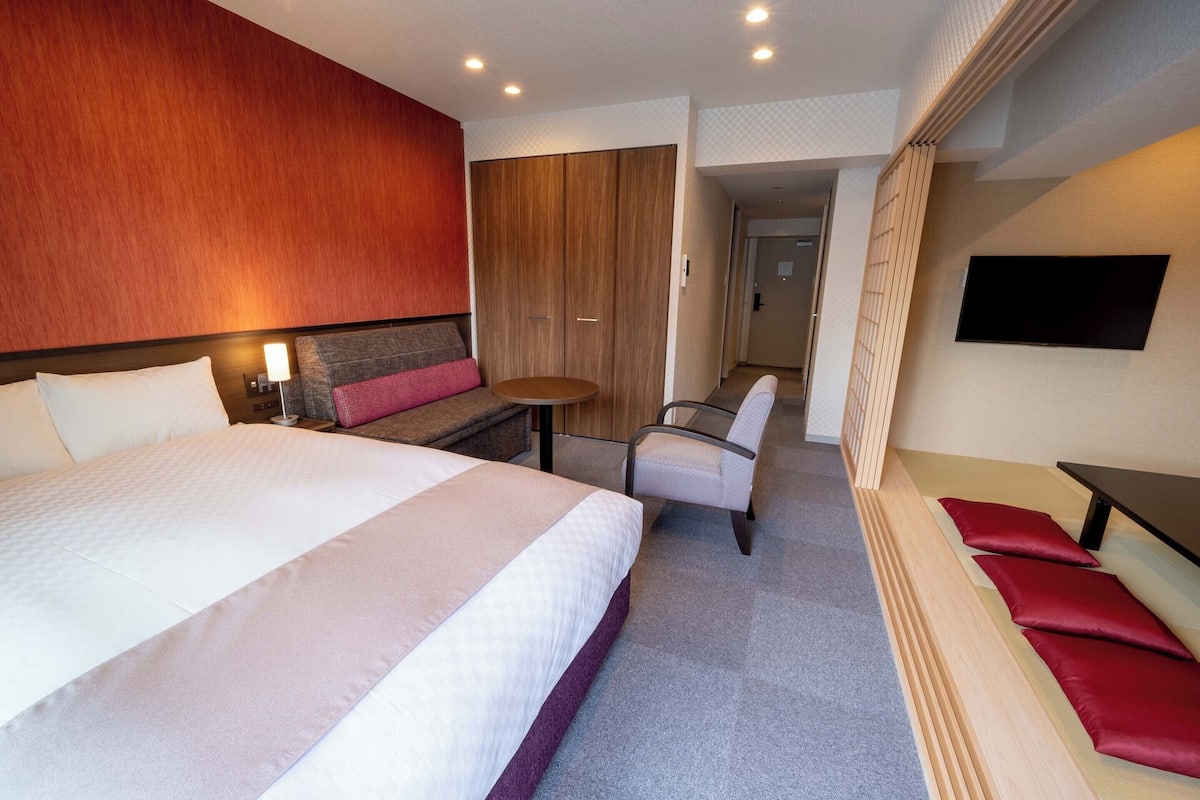 Ein Hotelzimmer mit einem großen Bett, einem Schreibtisch, einem Stuhl, einem Fernseher und einem Kleiderschrank.
