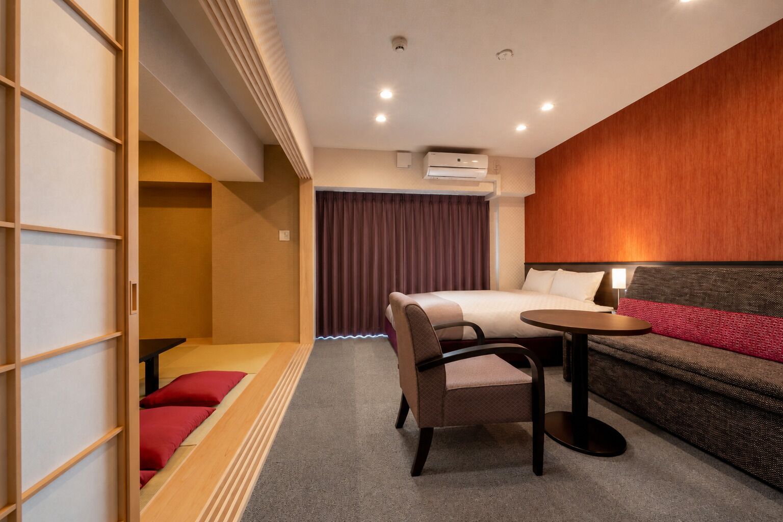 A hotel room with a bed, a sofa, a small table, a chair, and a wardrobe.