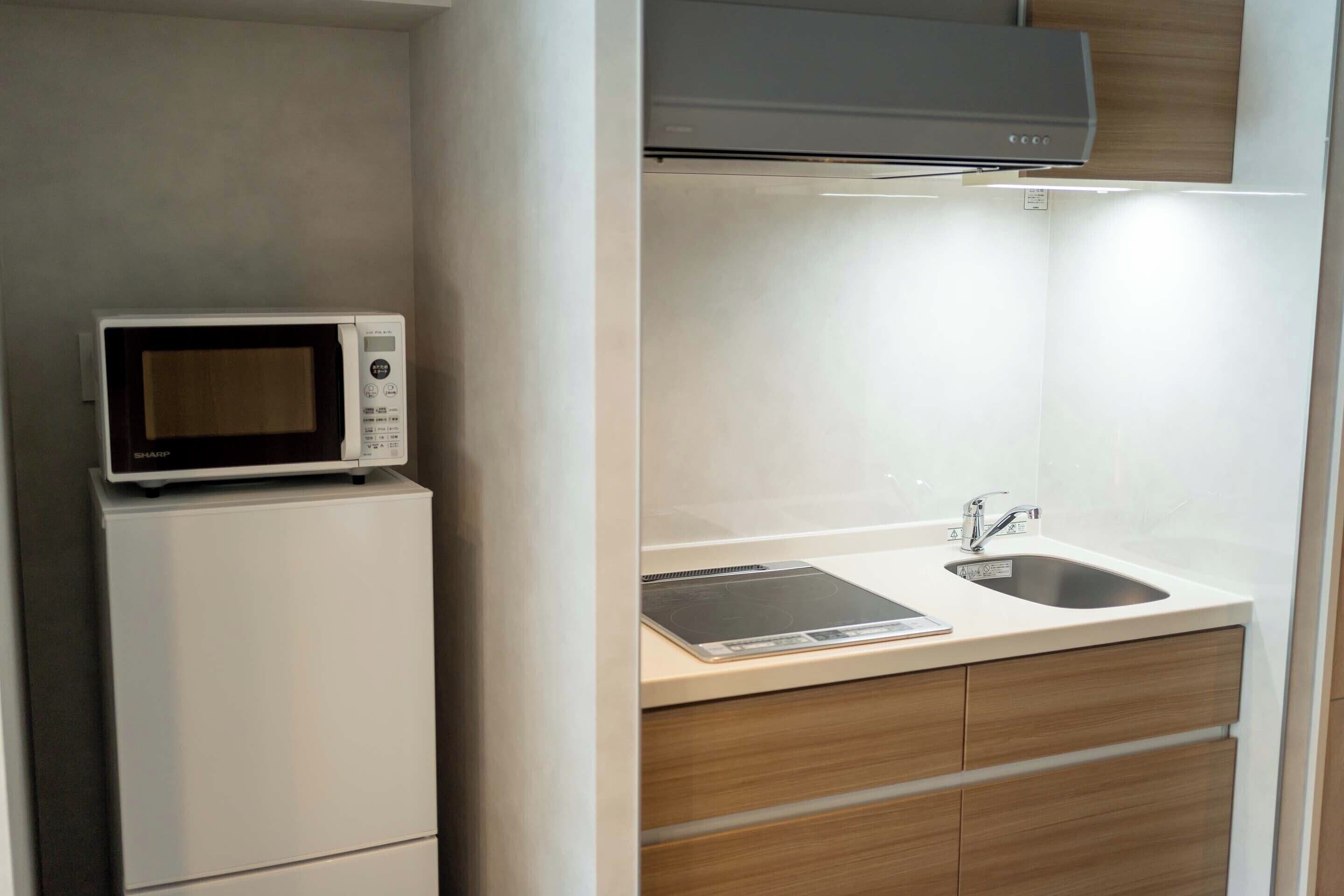 A compact kitchen with a microwave on a small fridge, a sink with a faucet, and wooden cabinets.