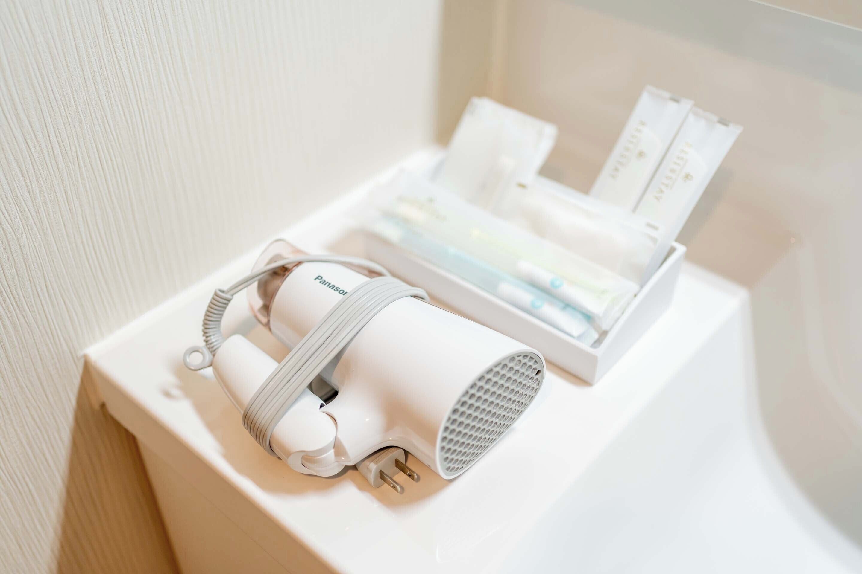 Un dispositivo portátil blanco sobre una superficie blanca, posiblemente una habitación de hotel, con un cable de carga y una caja con documentos.