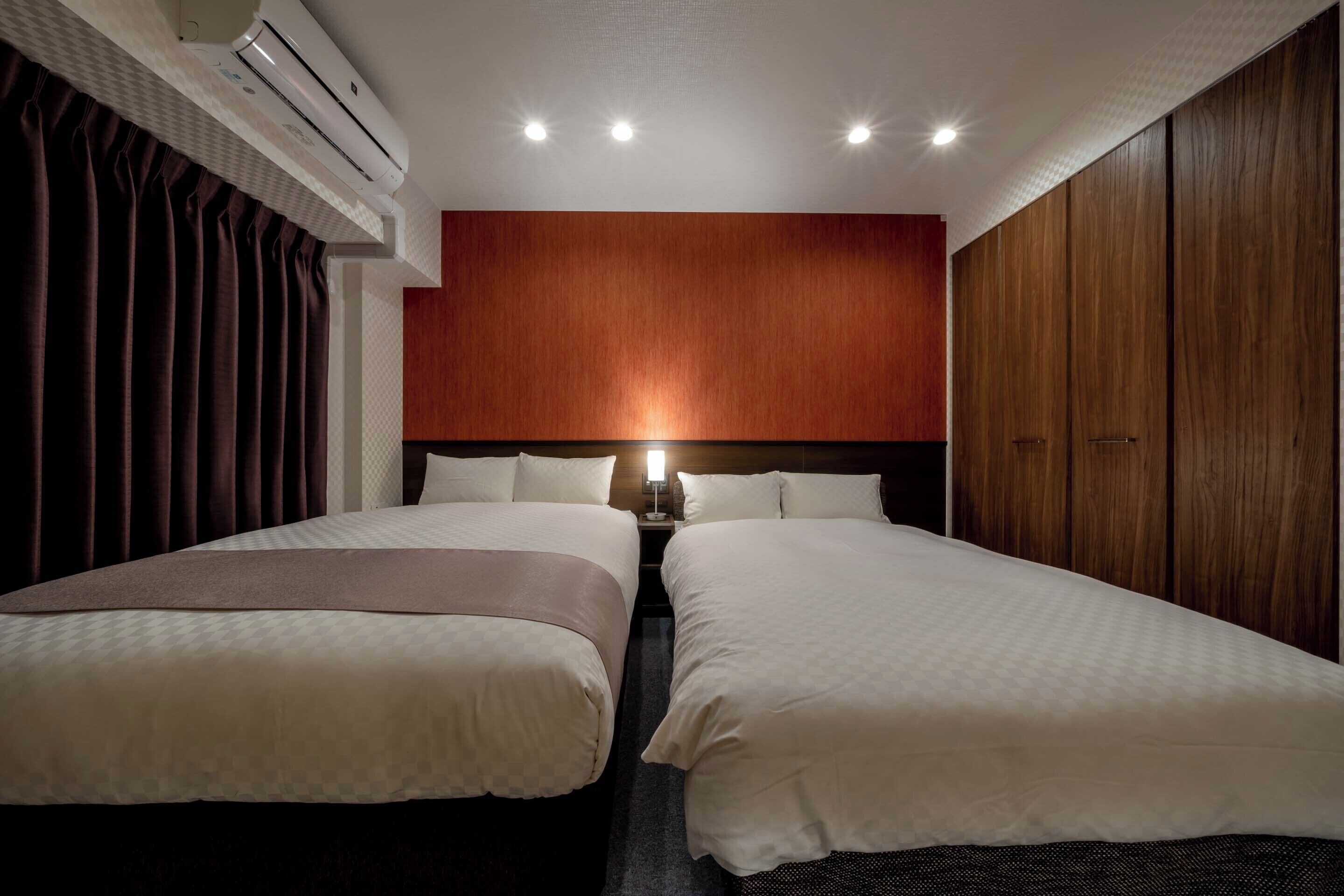 Ein Hotelzimmer mit zwei Betten, einem Holzkopfteil, einer Klimaanlage und einem Nachttisch mit einer Lampe.