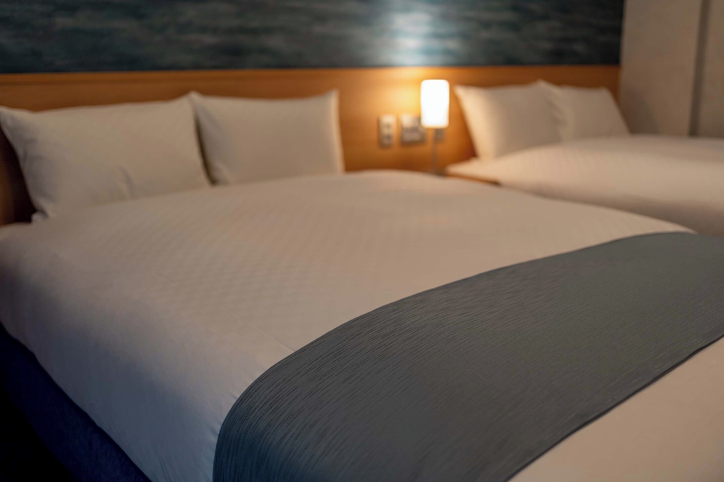 A hotel room with a large bed, a nightstand with a lamp, and a headboard with a textured wall behind it.