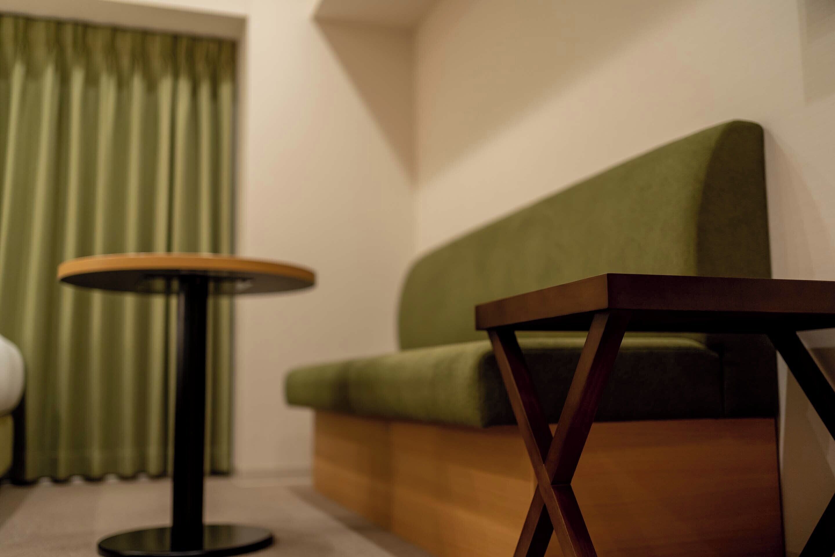 A room with a green sofa, a round table, and a window with curtains.