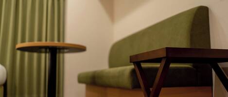 A room with a green sofa, a round table, and a window with curtains.
